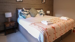 A neatly made bed with a patterned blanket, two pillows, and a bedside lamp on a wooden nightstand. - Cader Cottage (Dolgellau)