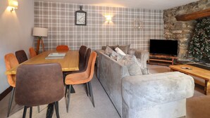 A modern living room with a plaid wallpaper, a fireplace, a television, and a dining area with a wooden table and chairs. - Cader Cottage (Dolgellau)