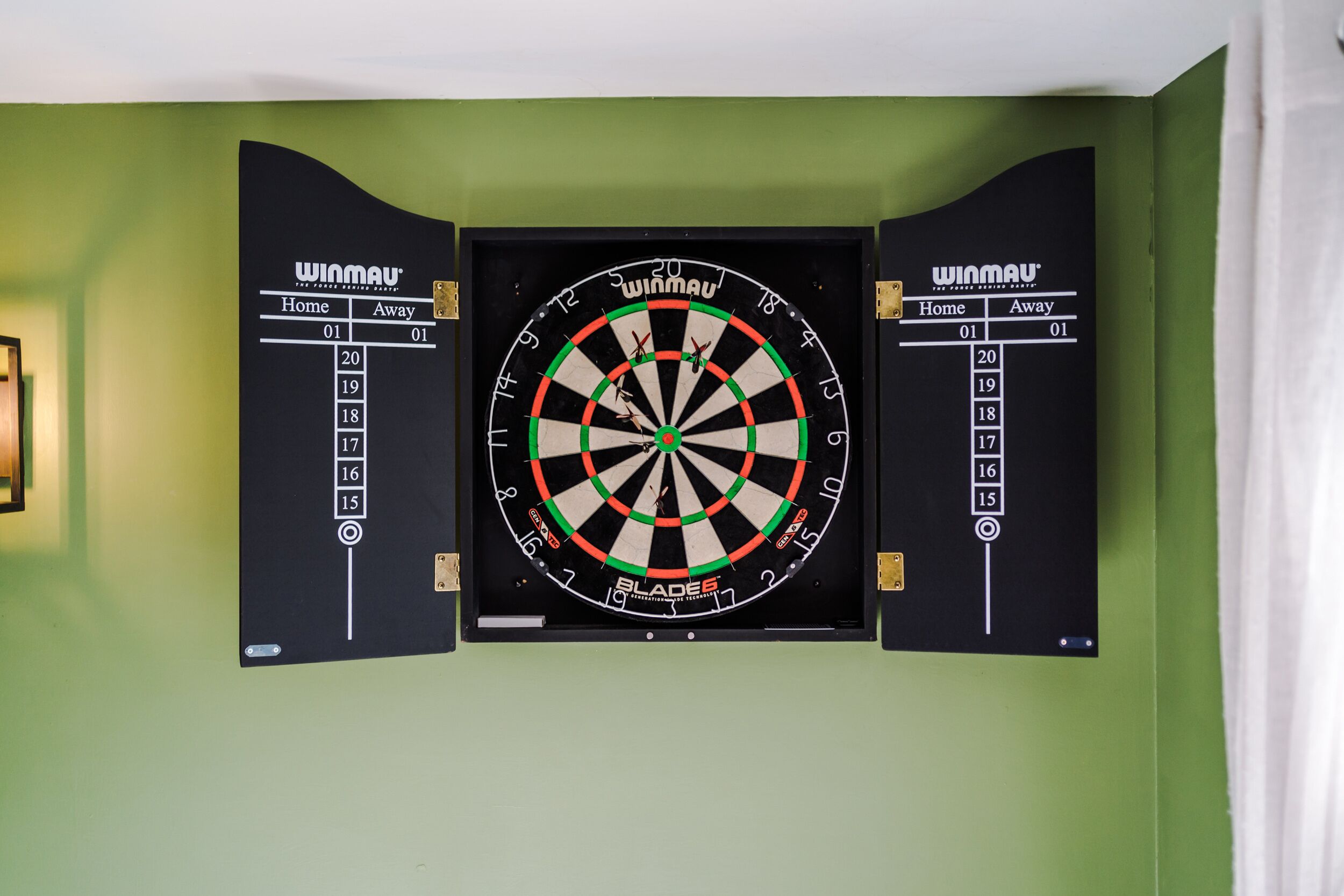 A dartboard mounted on a green wall with a score chart on either side.