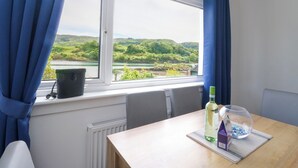 A room with a window overlooking a green landscape, a table with a bottle and a glass, and a radiator. - 3 Whin Bank (Oban)