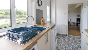 A kitchen with a double sink, a clock on the wall, and a view of greenery outside. - 3 Whin Bank (Oban)