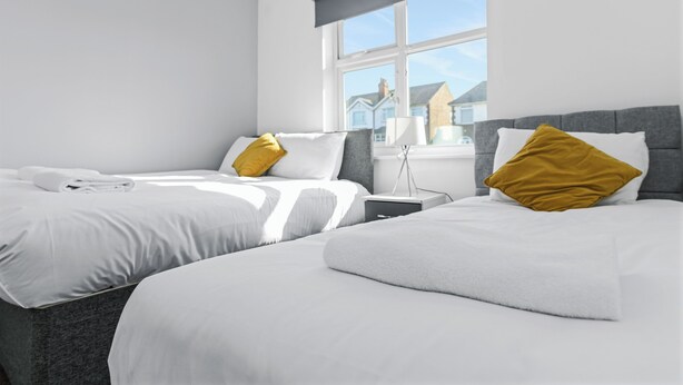 A modern hotel room with two beds, a nightstand, and a window with a view of houses.