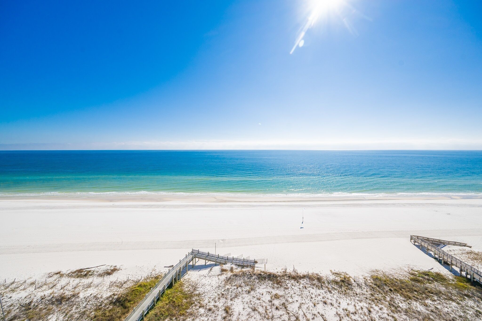 Ein Strand mit einer Holzpromenade, die zum Wasser führt, bewölkter Himmel und ruhiges Meer.