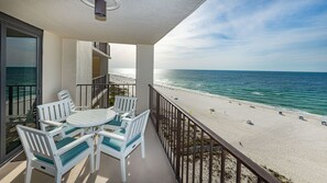 Un balcon avec une table et des chaises, donnant sur une plage et offrant une vue dégagée sur l’océan.