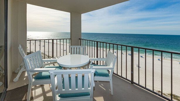 Ein Balkon mit Tisch und Stühlen mit Blick auf einen Strand und einer Geländer.