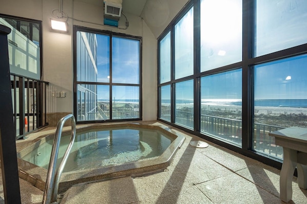 Uma grande piscina interior com barreira de vidro, amplas janelas e vista para a praia.