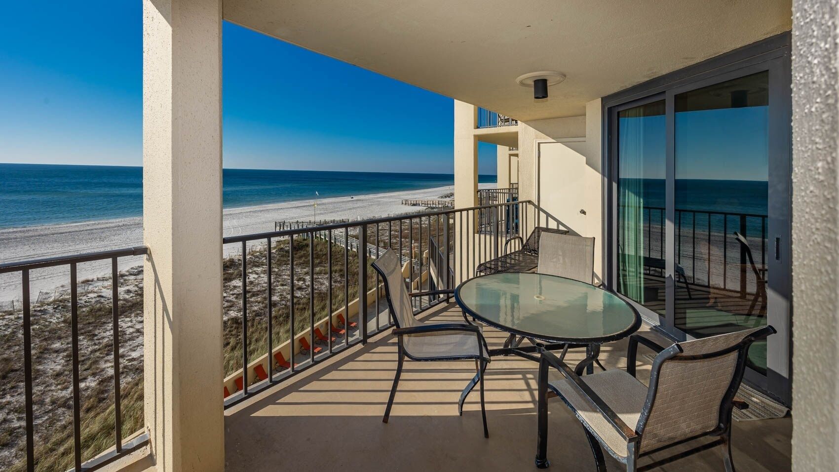 Ein Balkon mit Glastisch und Stühlen, mit Blick auf einen Strand.