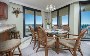 A dining area with a glass table and wicker chairs, overlooking a balcony with a view of the ocean. - Phoenix Iii 3049 3 Bedroom Condo (Orange Beach)