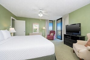A hotel room with a bed, a television, a chair, a desk, and a balcony with curtains. - Phoenix Iii 3049 3 Bedroom Condo (Orange Beach)