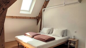 A bedroom with a sloped ceiling, a skylight, a bed with white and pink bedding, a small bedside table with a lamp, and an air conditioning unit. - Gîte Prétanie - Pondside healthy lodging in lively Piégut-Pluviers (Piégut-Pluviers)