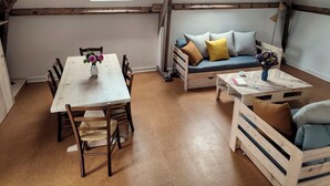 A cozy loft-style room with a wooden dining table, a sofa with cushions, a small wooden coffee table, and a window with a view. - Gîte Prétanie - Pondside healthy lodging in lively Piégut-Pluviers (Piégut-Pluviers)