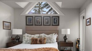 A bedroom with a bed, a skylight, framed pictures, and a nightstand with a lamp. - Saddle Ridge B5 3 Bedroom Townhouse (Big Sky)