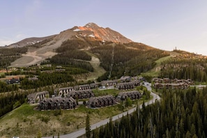 A resort with multiple chalet-style buildings, a ski trail, and a mountain backdrop. - Saddle Ridge B5 3 Bedroom Townhouse (Big Sky)