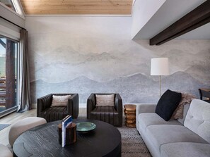 A modern living room with a mountain mural, leather sofas, a round coffee table, and a floor lamp. - Saddle Ridge B5 3 Bedroom Townhouse (Big Sky)