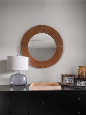 A round mirror with a wooden frame on a wall, a grey lamp beside it, and a black dresser with drawers. - Saddle Ridge B5 3 Bedroom Townhouse (Big Sky)