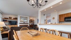 A modern living room with a wooden dining table, sofas, and a kitchen area with wooden cabinets and a microwave. - 100 Snow Creek 2 Bedroom Condo (Warren)