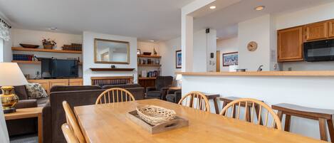 Una sala de estar moderna con una mesa de comedor de madera, sofás y una zona de cocina con armarios de madera y un microondas.
