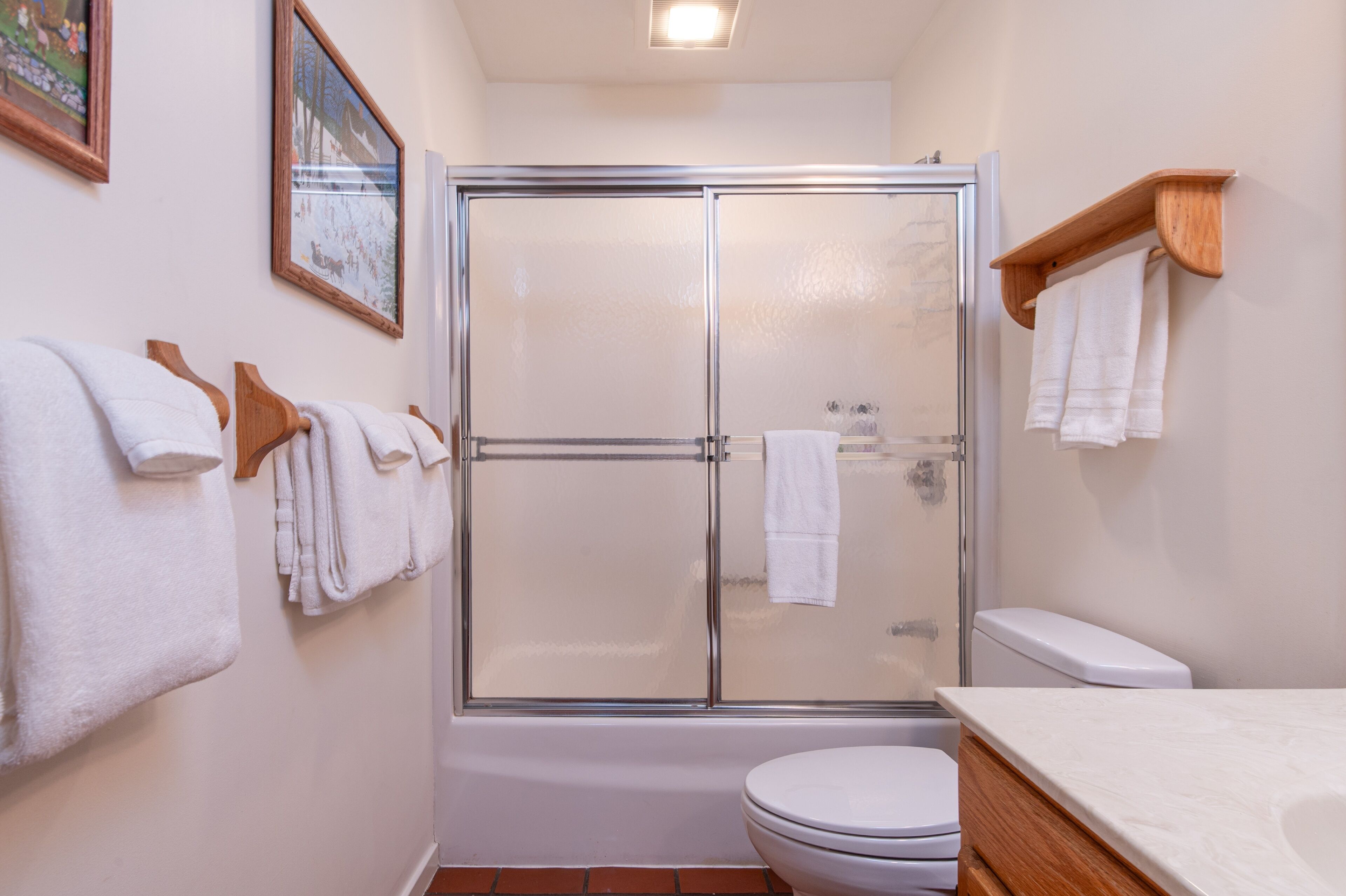 A bathroom with a glass-enclosed shower, a white toilet, and a wooden shelf with towels.