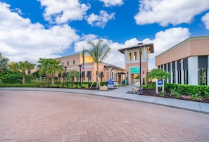 A hotel entrance with a paved driveway, palm trees, and a clear blue sky. - New! Modern Townhome Near Disney! Splash Pool, Resort W/waterpark-8206sa 3 Bedroom Townhouse (Kissimmee)