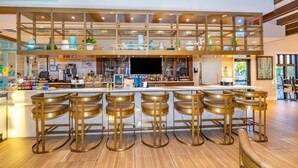 Uma área de bar com teto alto, vários níveis e diversas opções de assento, incluindo banquetas e um banco.