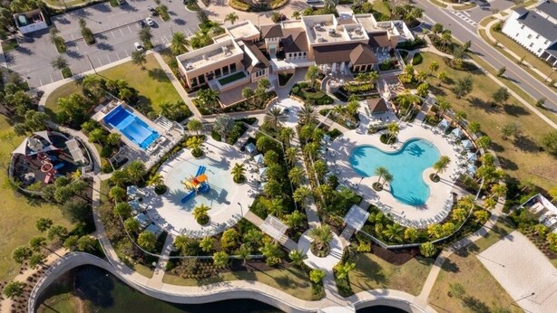 Vista aérea de um resort com várias piscinas, uma ponte e uma área ajardinada com palmeiras.