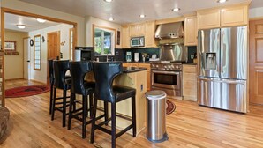 A modern kitchen with wooden cabinets, stainless steel appliances, and a bar area with stools. - Otter Run 3 Bedroom Home (Bend)