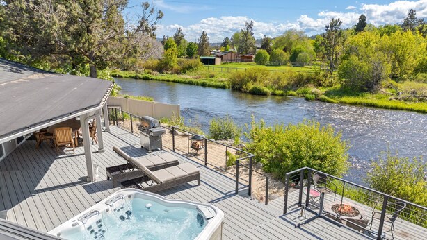 A deck with a hot tub, lounge chairs, and a fire pit overlooking a river. - Otter Run 3 Bedroom Home (Bend)