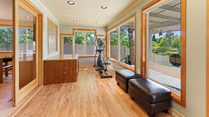 A spacious room with wooden flooring, large windows, and exercise equipment. - Otter Run 3 Bedroom Home (Bend)