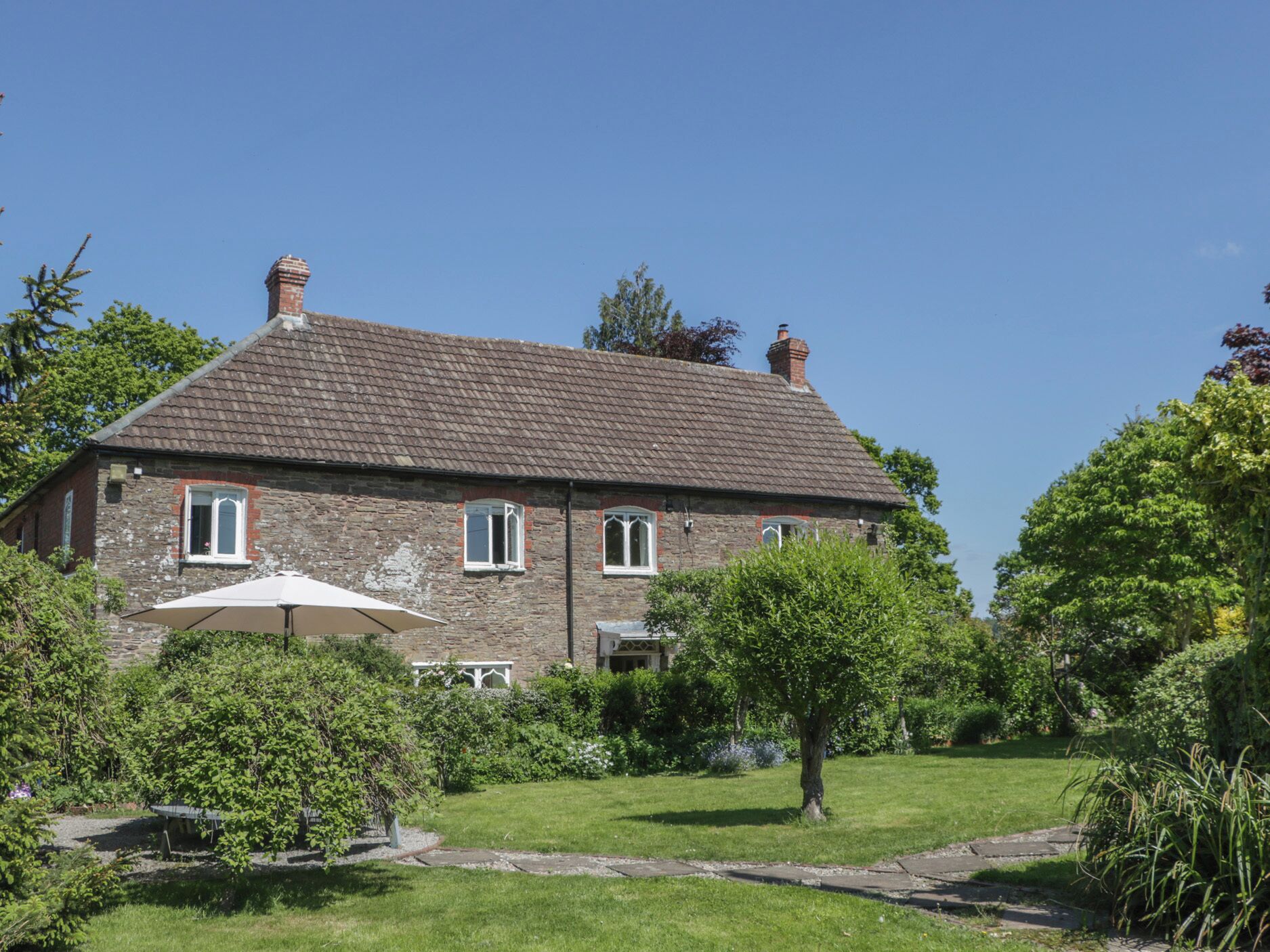 A stone house with a tiled roof, a garden with a lawn, and a white umbrella.