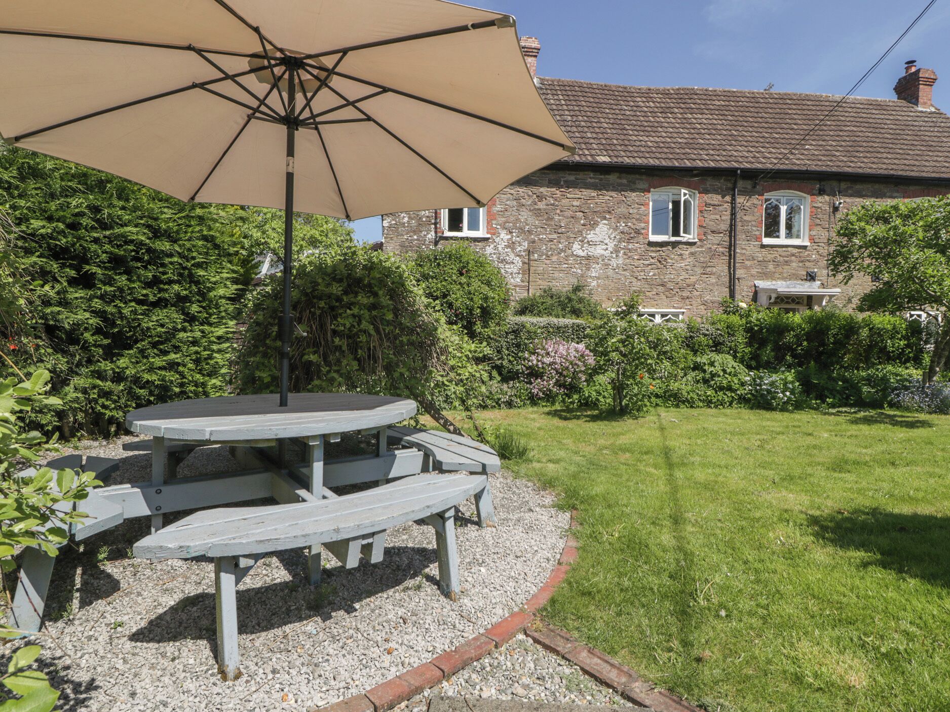 A picnic table with a canopy in a garden area with a stone building in the background.