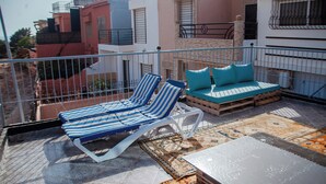 Eine Dachterrasse mit Liegestühlen, einer Sitzecke und einem Teppich mit Muster, sowie einem Metallgeländer.