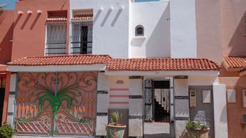 A building with a white facade, a red-tiled roof, and a green wrought iron gate.