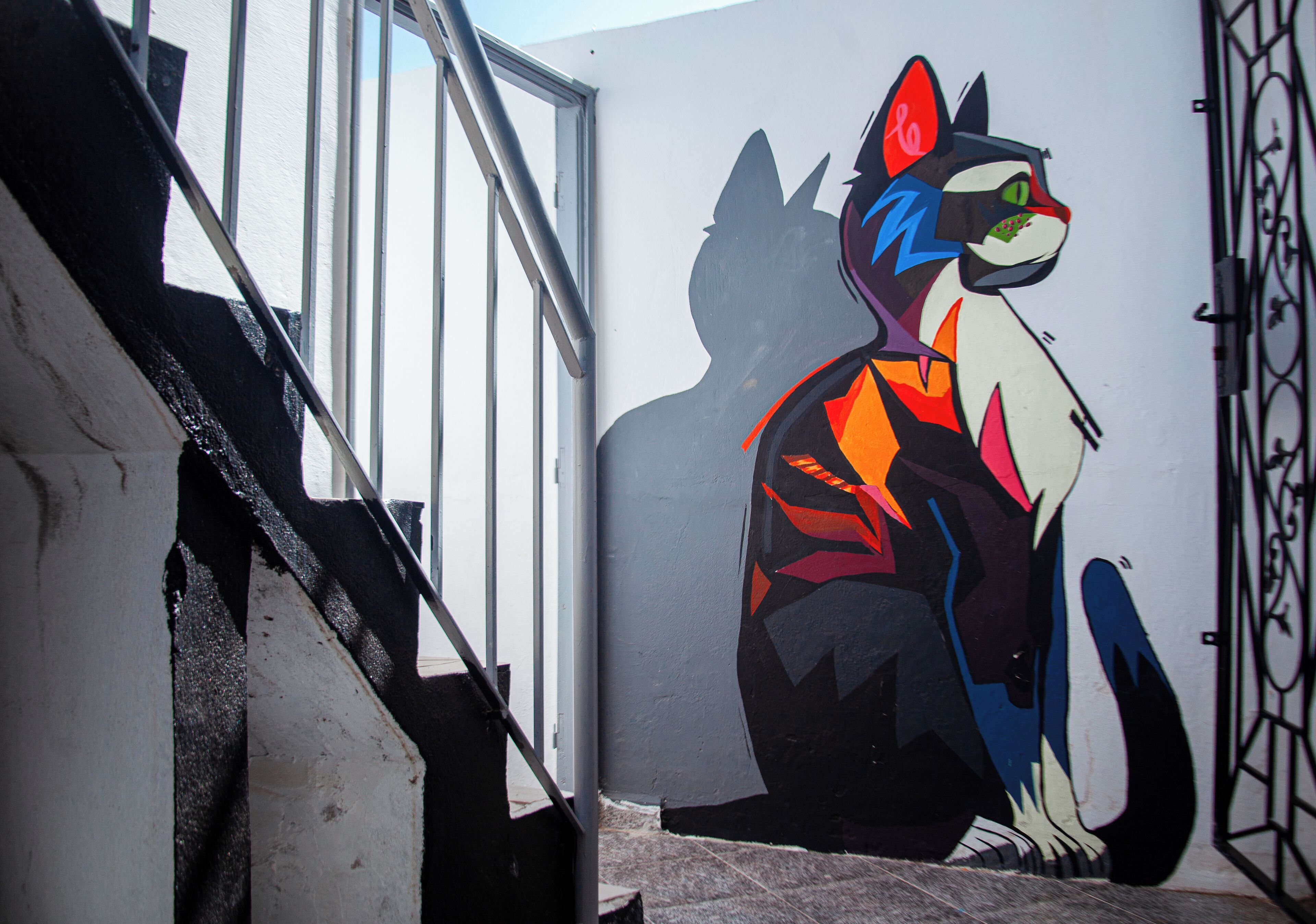 A mural of a stylized cat on a wall next to a staircase.
