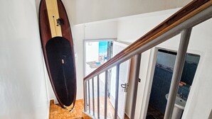 Eine Treppe mit einem Surfbrett, das an der Wand lehnt, führt zu einem Raum mit Fliesenboden und einer Tür.