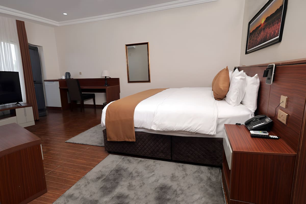 A hotel room with a bed, bedside table, TV, desk, chair, and a large window with curtains.