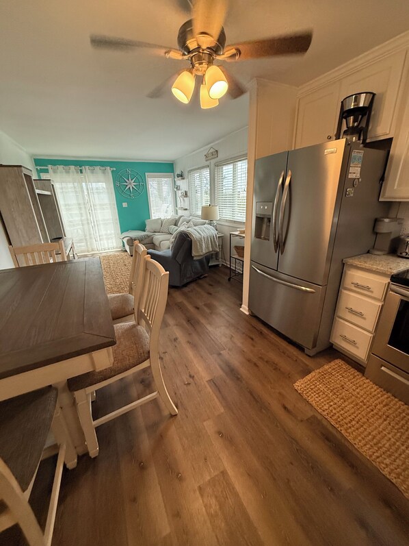 A modern kitchen with a central island, stainless steel appliances, and a dining area with a wooden table and chairs. - Cozy Unit at Oceanfront Complex, Pool & Steps from Ocean by Williamson Realty (Ocean Isle Beach)