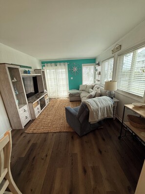 A living room with a sofa, TV, and a rug. - Cozy Unit at Oceanfront Complex, Pool & Steps from Ocean by Williamson Realty (Ocean Isle Beach)