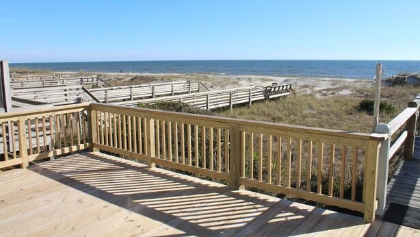 A wooden deck with a view of the beach and ocean.