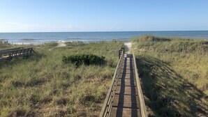 A wooden boardwalk leading to the beach, surrounded by grass and dunes.