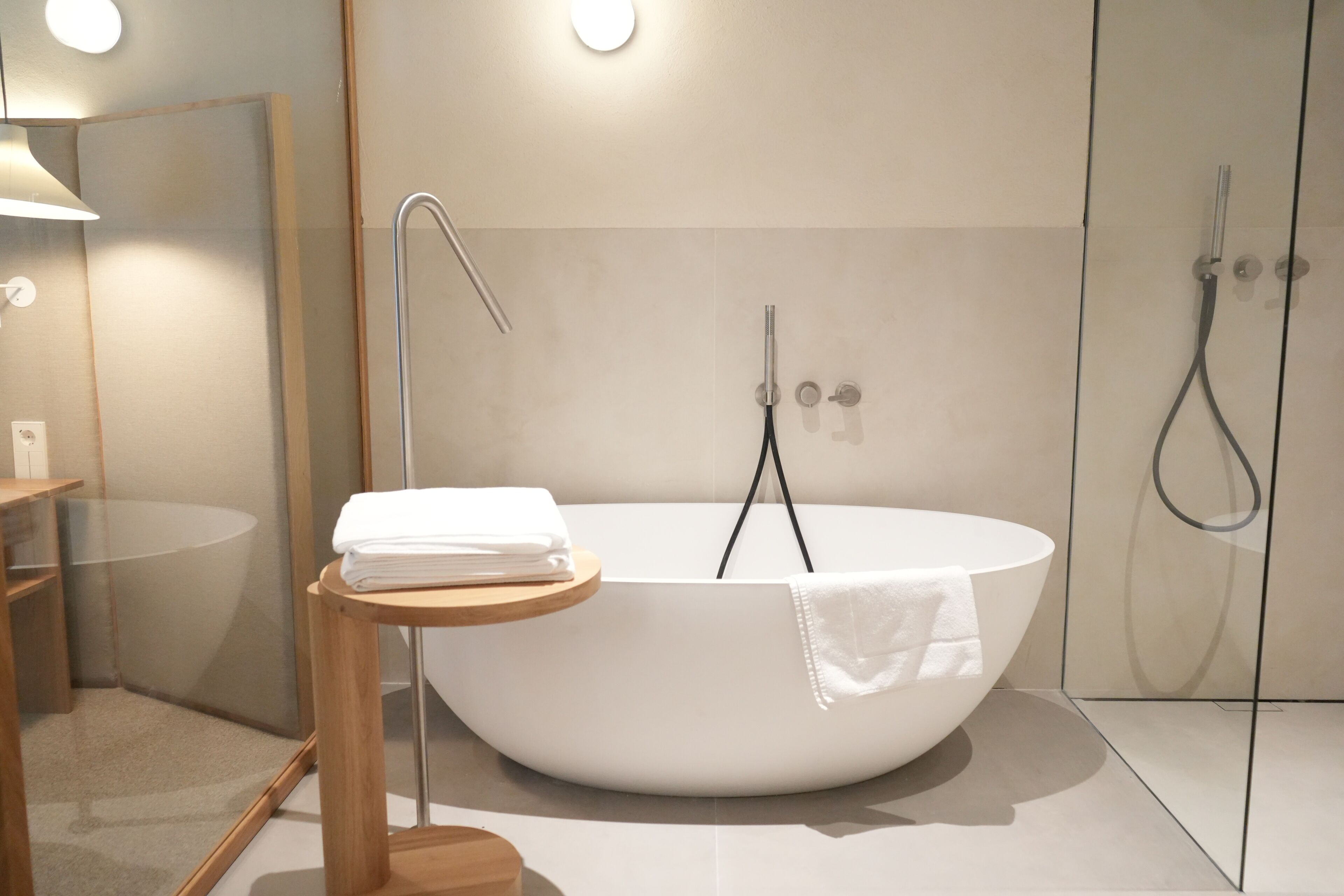 Une salle de bain moderne avec une baignoire sur pieds, un petit tabouret en bois avec des serviettes et une cabine de douche en verre.