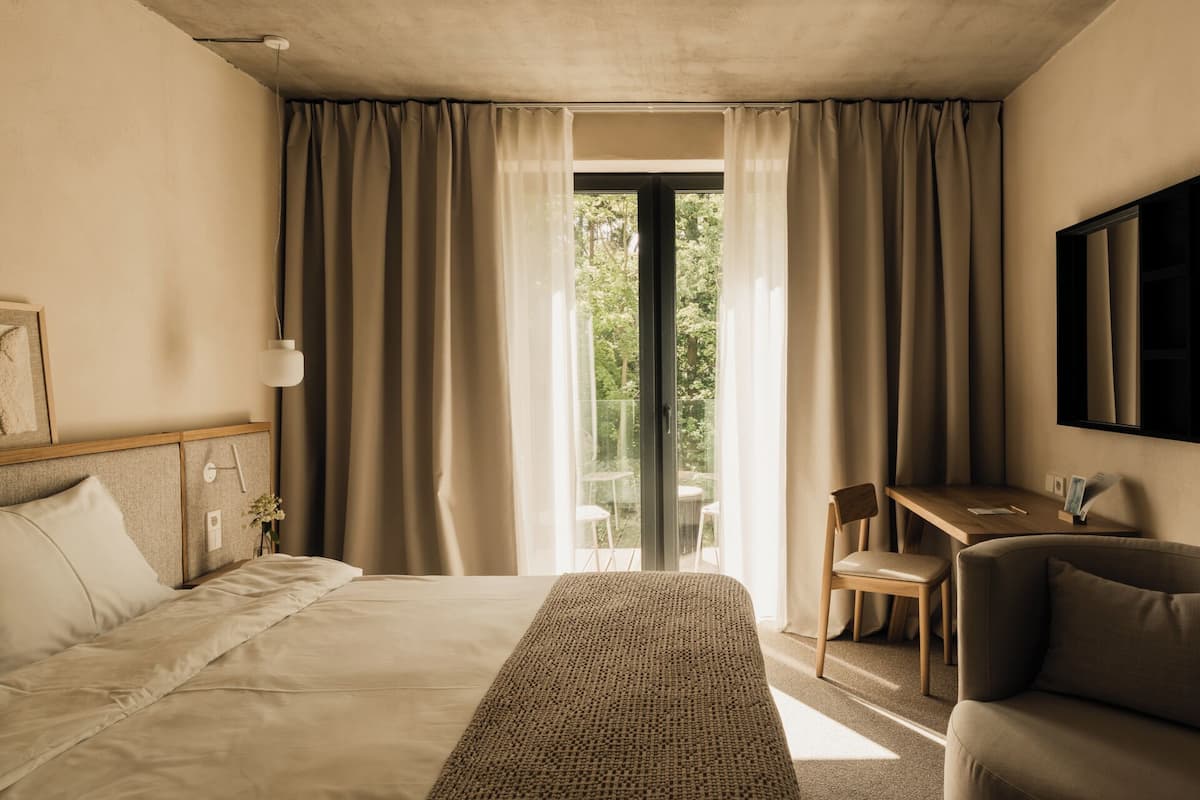 Habitación de hotel con cama, escritorio, silla y vista a través de una puerta de vidrio.