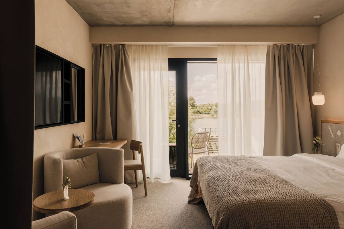 Habitación de hotel con cama, escritorio, silla y vista al lago a través de la ventana.