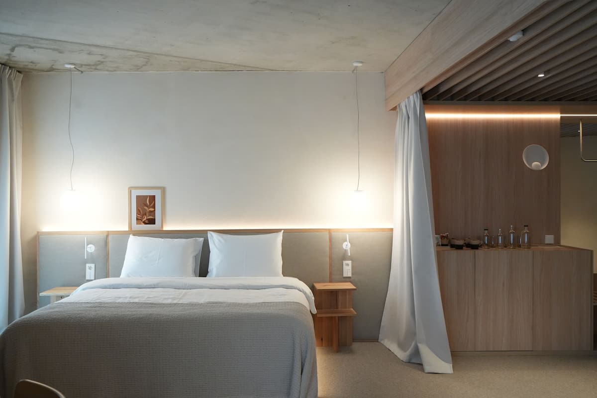 Una habitación de hotel moderna con una cama grande, mesitas de noche, un armario de madera y un área de baño.
