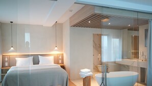 A modern hotel room with a large bed, bedside lamps, a glass shower enclosure, and a freestanding bathtub. - At Hotel 35 (Słupca)