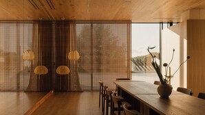A modern dining area with a wooden table and chairs, a decorative plant, and a view through a wooden partition. - At Hotel 35 (Słupca)
