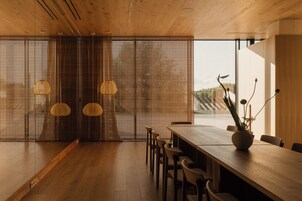 Un espace repas moderne avec une table et des chaises en bois, une plante décorative et une vue à travers une cloison en bois.