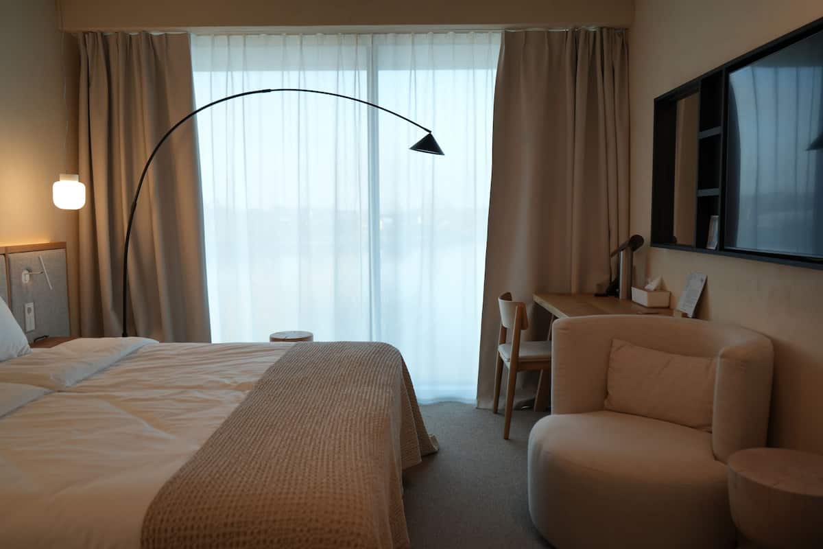 Una habitación de hotel con cama, escritorio, silla y un ventanal con cortinas.