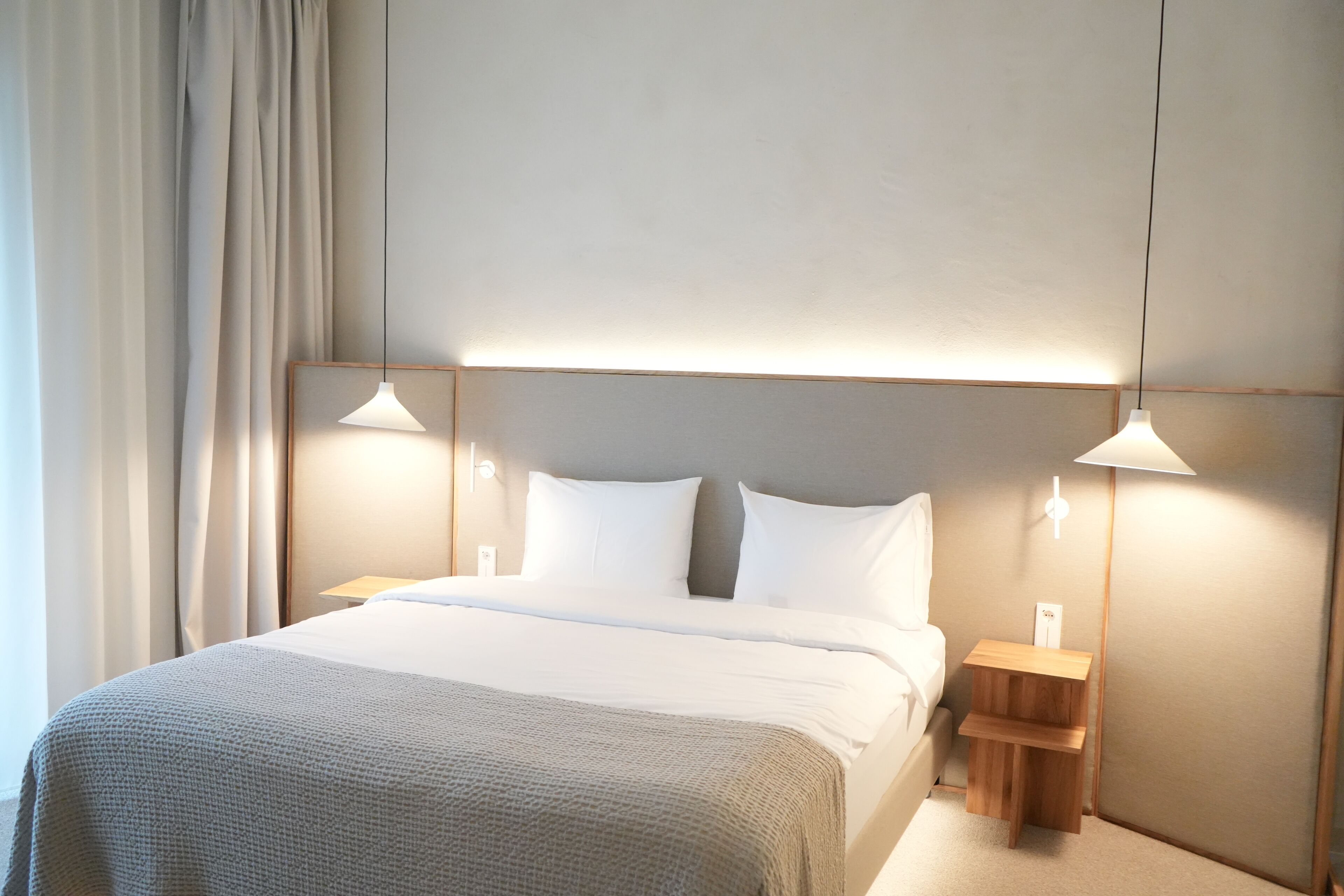 Ein modernes Hotelzimmer mit einem großen Bett, zwei Nachttischen und Pendelleuchten.