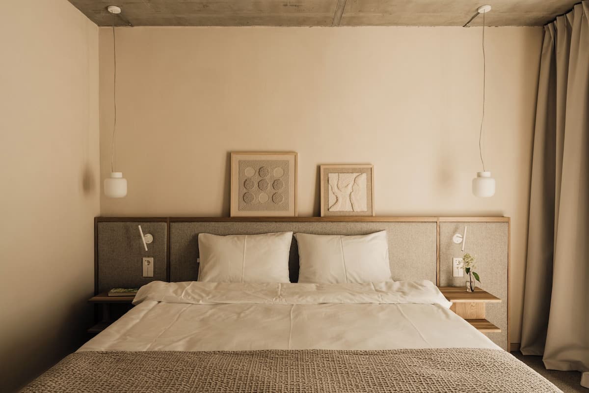 Una cama bien hecha con un edredón texturizado, dos mesitas de noche con lámparas y dos cuadros enmarcados en la pared.
