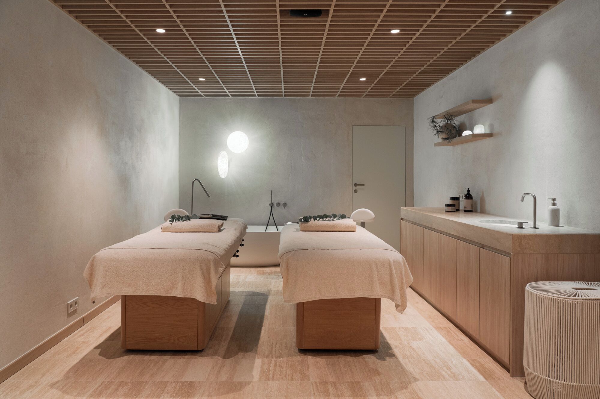 Een moderne spa ruimte met twee houten bedden, een houten kast en een wastafel met toiletartikelen.